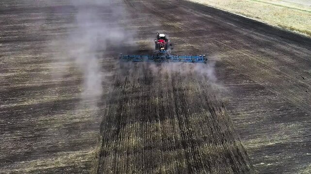 Experience the dynamic movement of a red tractor as it plows through dusty terrain. This aerial footage highlights the intricate dance of machinery and nature working in harmony. Aerial FHD footage.