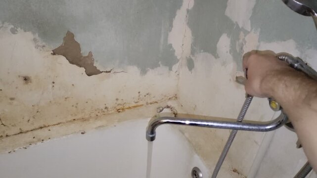 Person turning on water faucet in old dirty moldy bathtub with peeling plaster, vertical video