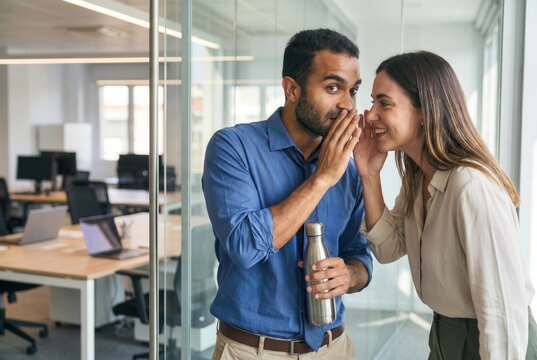 Diverse business colleagues whispering secret while gossiping during work break in office