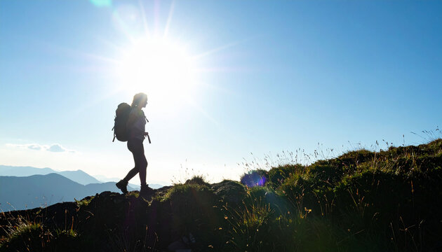 登山する女性のシルエットと輝く太陽の光　山の頂上を目指すハイカーと青空の広大な風景写真　冒険や挑戦をイメージさせるアウトドアアクティビティの背景素材　コピースペースのある自然の広がり