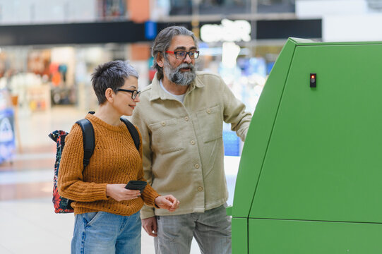 Senior couple using modern atm terminal at mall