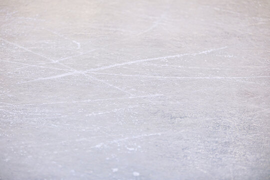 Rough texture of a frozen ice rink surface showing many white skate marks and scuffs from winter sports