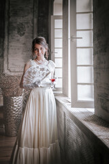 Obraz premium Elegant woman in vintage white gown by window in classic interior