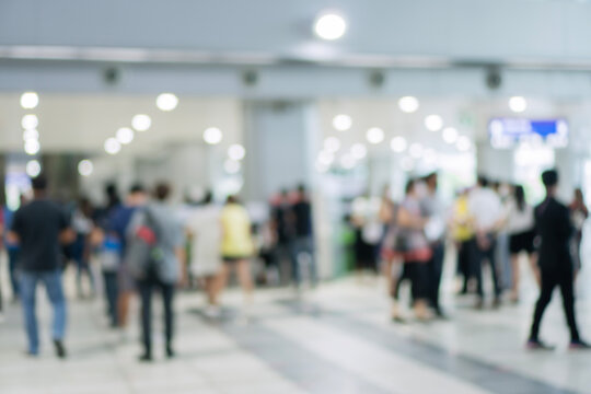 Blurred background of abstract unrecognizable crowd of people standing and walking in a modern public building, airport, or hospital. Defocused interior space with bright bokeh light.