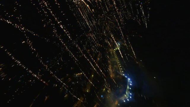 FPV aerial view of fireworks exploding over the city skyline at night with glowing lights in Novi Sad, Vojvodina, Serbia.