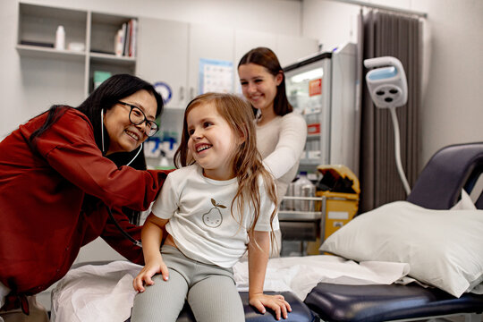 Asian doctor warmly interacts with the young girl as she examines her with stethoscope