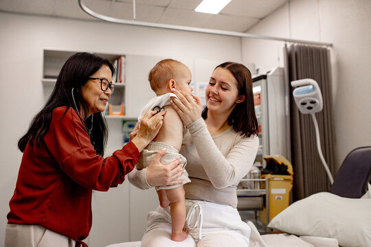 Doctor performing paediatric examination with stethoscope while the mother holds her baby