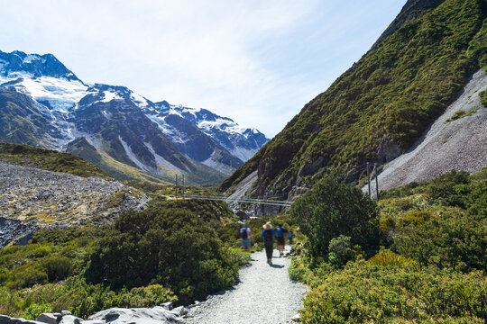 People walking along a track in a glacial valley with snow capped mountains