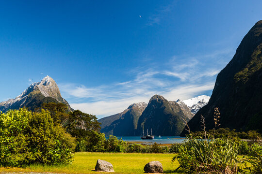 View across shrubs and yellow grasses to blue water with boat and spectacular mountain peaks