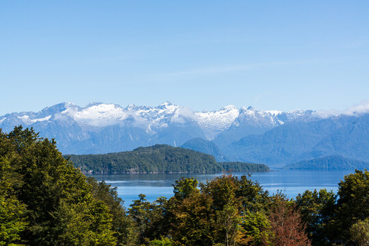 View from a high point to a blue body of water with snow capped mountains in the background