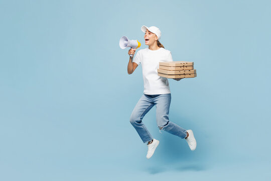 Full body delivery employee woman wear white T-shirt uniform work as dealer courier hold pizza in cardboard flatbox jump scream in megaphone isolated on plain blue background studio. Service concept.