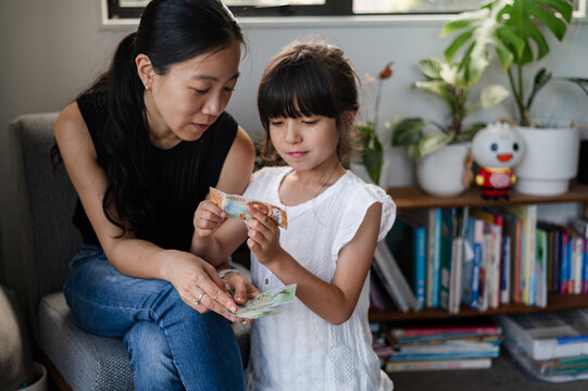 A woman shows a young girl different banknotes in a warm, home environment