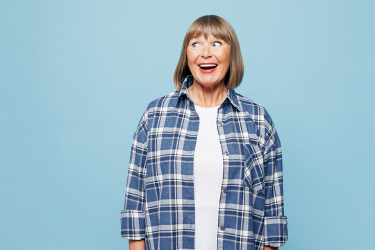 Elderly shocked surprised excited blonde woman 50s years old wears checkered shirt casual clothes look aside on area isolated on plain pastel light blue background studio portrait. Lifestyle concept.