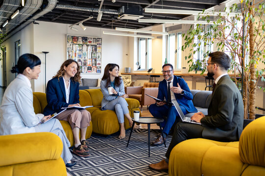 Diverse executive team brainstorming and sharing ideas while casually sitting on sofas in a vibrant office relaxation area