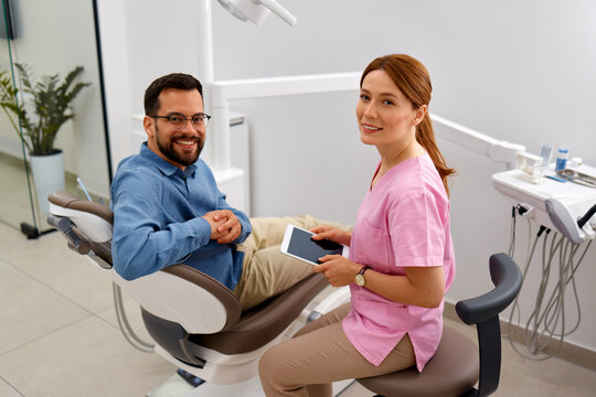 Happy male patient sitting in dental chair with female dentist after successful dental consultation.