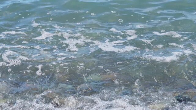 Rippling blue sea water surface texture and pebble shore.