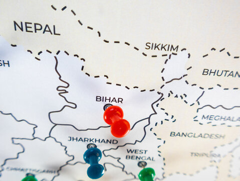 Close-up of a regional map featuring eastern India, Nepal, and Bhutan. Colorful push pins in red, blue, and green mark specific locations, with selective focus creating a shallow depth of field.