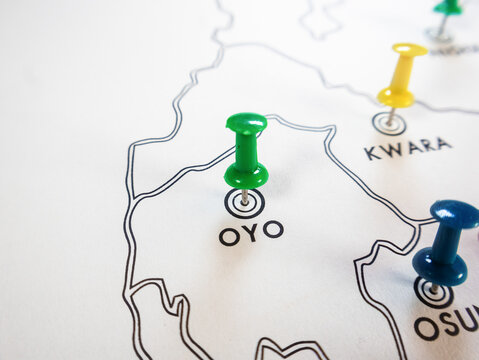 A close up shot of a white Nigerian state map. Brightly colored pushpins green, yellow, and blue mark specific southwestern states including Oyo, Kwara, and Osun to pinpoint precise locations.