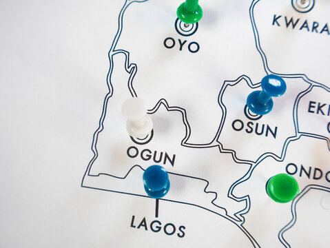 A close up shot of a white Nigerian state map. Brightly colored pushpins blue, green, and red mark specific southwestern states including Lagos, Osun, Oyo, and Ondo.