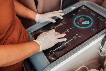 Obraz premium Aesthetic technician adjusting settings on an electromagnetic muscle stimulation device before a body contouring treatment session.