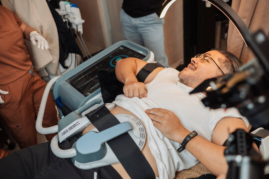 Overweight middle aged male client undergoing a noninvasive electromagnetic muscle stimulation treatment on the abdomen at an aesthetic clinic.