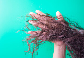 Naklejka premium woman's hand with long brown hair on a green background close up