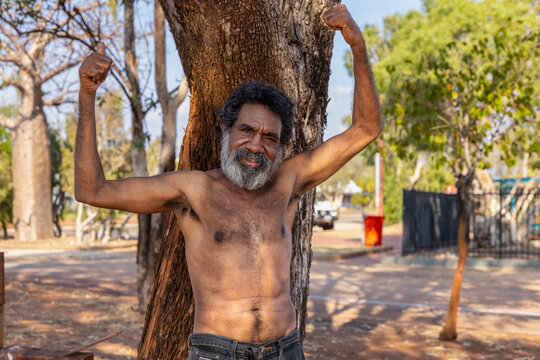 middle-aged aboriginal man with arms in the air flexing biceps with thumbs up