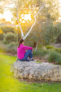 young woman in bright pink top sitting on rock facing away