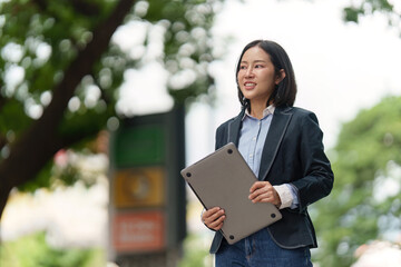 Fototapeta premium Asian woman in her 30s holding laptop outdoors, business professional