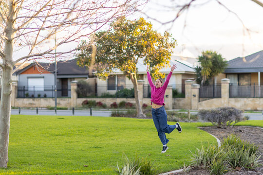 suburban park with young woman joyfully jumping
