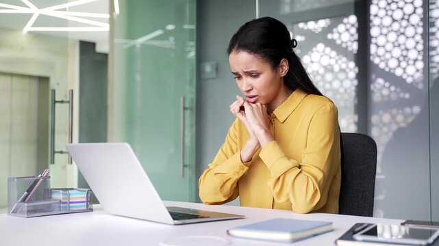 Depressed young businesswoman suffering from mental pain and headache while sitting at office desk. Desperate female employee feeling emotional distress and burnout at modern workplace near computer.
