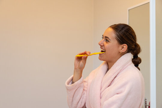 teen girl in pink dressing gown brushing her teeth in bathroom