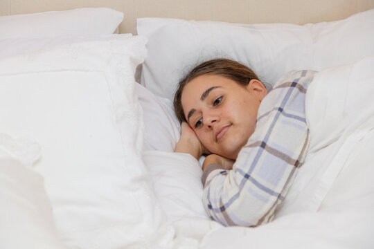 teenager snuggled up in bed with long-sleeved pjs and white bedlinen