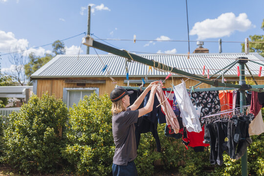 A teenager busy with household chores, hanging clothes to dry outdoors