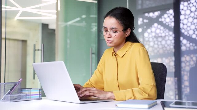 Confused young businesswoman working on laptop and looking at screen with doubt. Puzzled female employee having problems with computer or difficult task while sitting at modern corporate workplace.