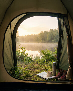 A paper map, thermos, and boots rest by the tent opening as sunrise over the misty lake sets a digital detox mood before the day begins.