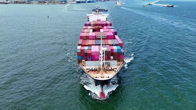 cargo ship fully loaded with pink and red containers, assisted by a tugboat in the turquoise ocean. Global maritime logistics and supply chain concept.	
