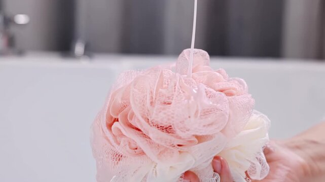 Unrecognizable young woman hand pours shampoo shower gel douche into bath mesh sponge, cleanliness bodycare, self-hygiene and healthcare using liquid soap product for cleaning body concept