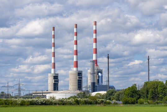 View of Kraftwerk Irsching power plant with its three tall red and white striped chimneys rising above green fields and trees in Vohburg an der Donau, Bayern, Germany.