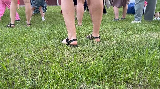 A group of people of different ages dancing together on green grass in summer, close-up of legs