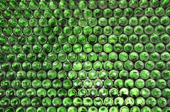 Full frame wall with empty green beer bottles bottoms. Alcohol theme. Endless rows of wine bottles. Green glass bottle wall with sunlight from behind