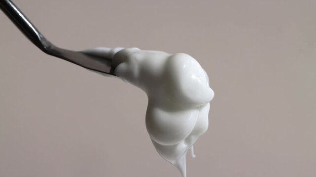 Sample of cosmetic hand cream, white face cream slips and falls down, macro, beige background.