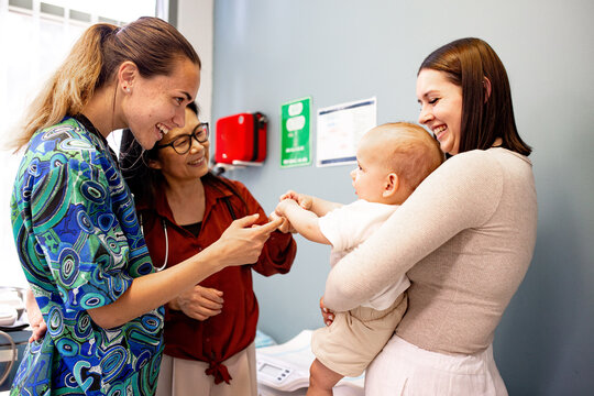 Two nurses happily interacting with baby and mother during clinic visit