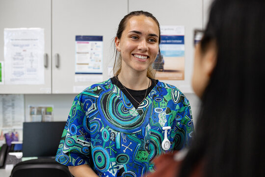 A nurse in patterned scrubs listening carefully to a fellow&rsquo;s concerns in a busy clinic