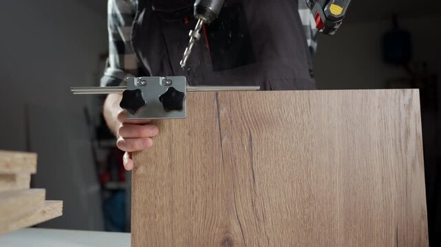 Person uses cordless drill with metal guide jig on wooden board in workshop. Woodworking carpentry and furniture assembly concept.