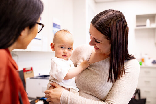 Baby showing curiosity while parent smiles and doctor in clinic