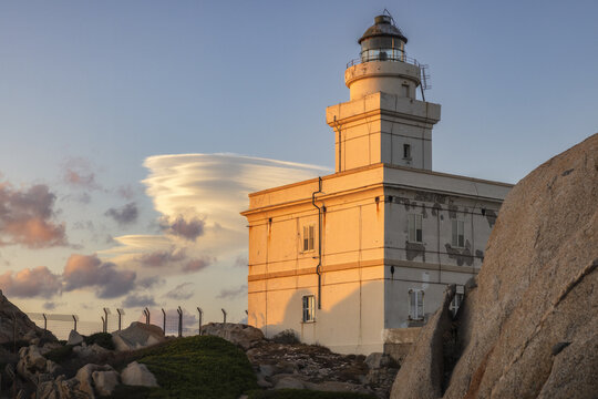 View of the Faro di Capo Testa lighthouse standing on rocky granite cliffs under a golden sunset sky with lenticular clouds Capo Testa, Sardegna, Italy.