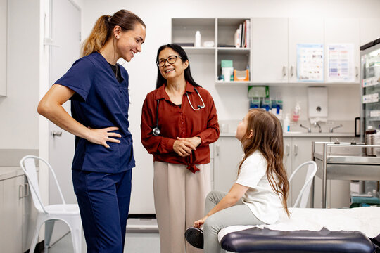 Two female healthcare professionals conversing with a child in medical examination room