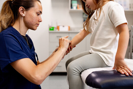 Female paediatric care professional examining child&rsquo;s wrist in clinic