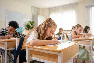 Diverse group of elementary students studying in classroom, Concentrated students writing at their desks in modern school, Children learning together in a bright primary school classroom © JU.STOCKER